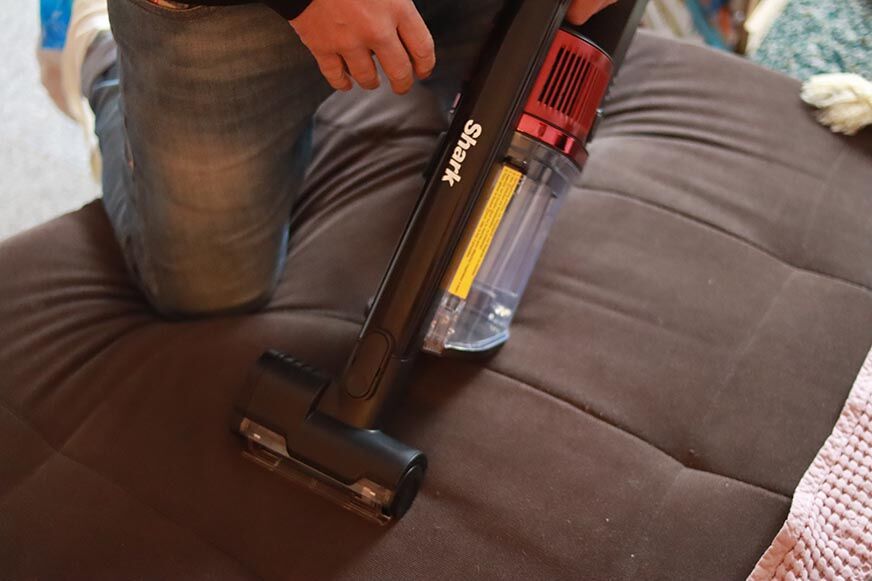 The Shark Anti Hair Wrap hand hoover is seen removing pet hair from furniture.